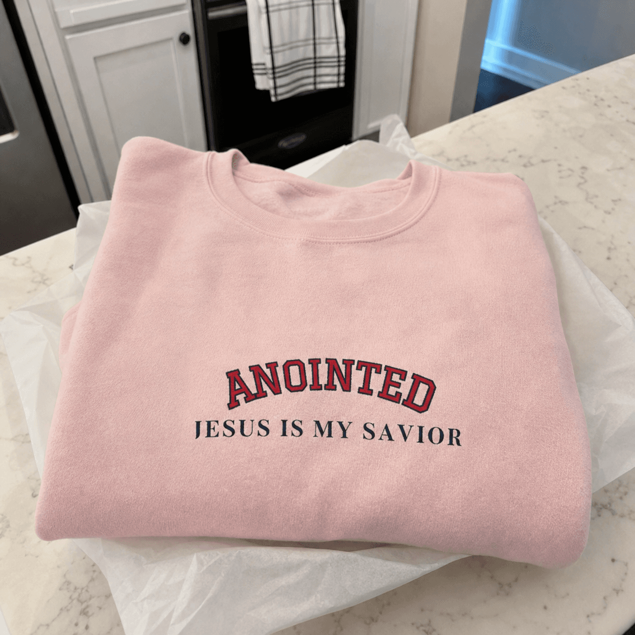 Folded light pink My Jesus sweatshirt on a kitchen counter